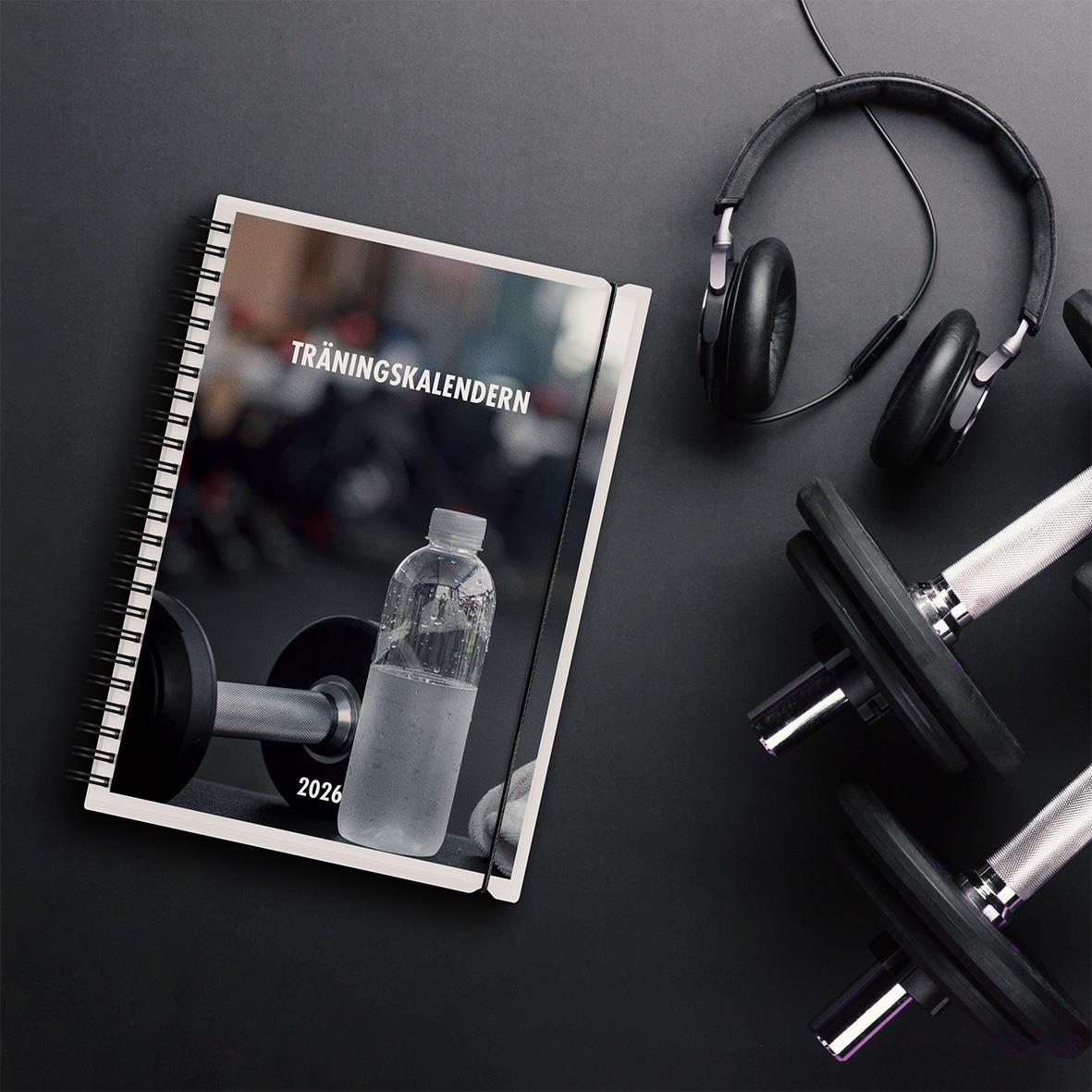Träningskalender 2026 i A5-format med träningsutrustning och hörlurar på en mörk bakgrund