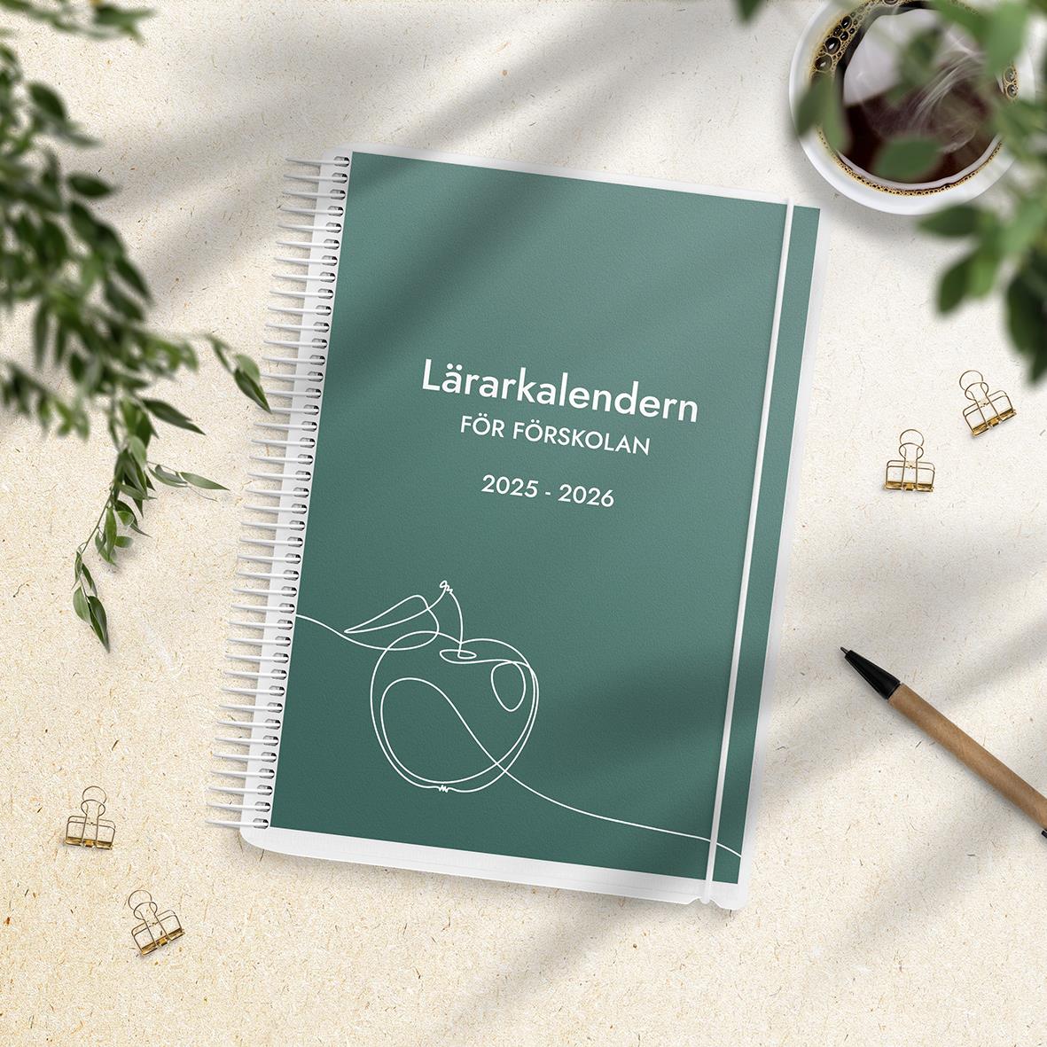 Lärarkalender för förskolan 2025-2026 med grön omslag och spiralbindning, omgiven av gröna växter, penna och klämmor