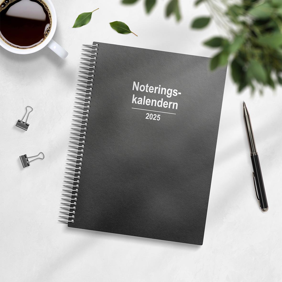 Noteringskalender 2025 i spiralbindning på skrivbord med pen, klämmor, kaffekopp och växt