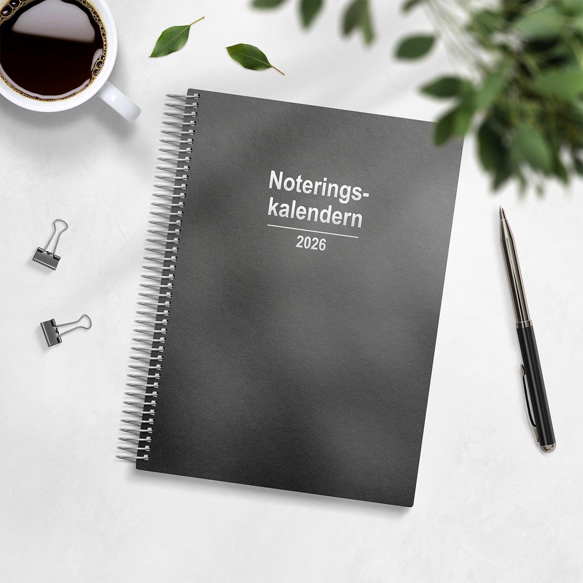 Noteringskalender 2026 refillkartong med spiralbindning på skrivbordet, omgiven av bläckpenna, koppar med kaffe och gröna blad