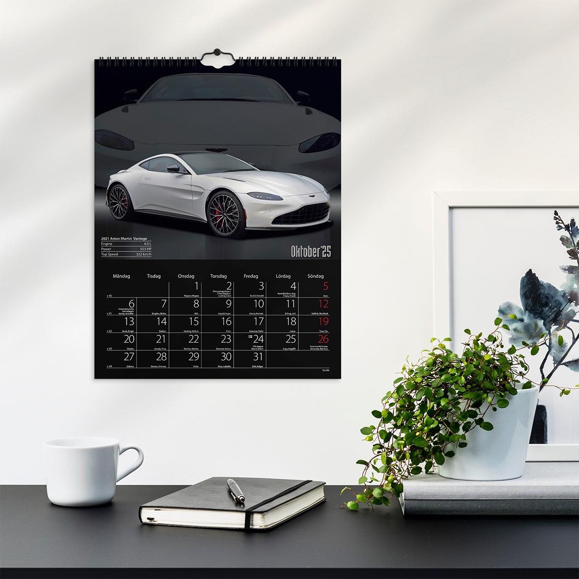 Väggkalender med bilmotiv för 2026 på en vit vägg bredvid växt och skrivbord