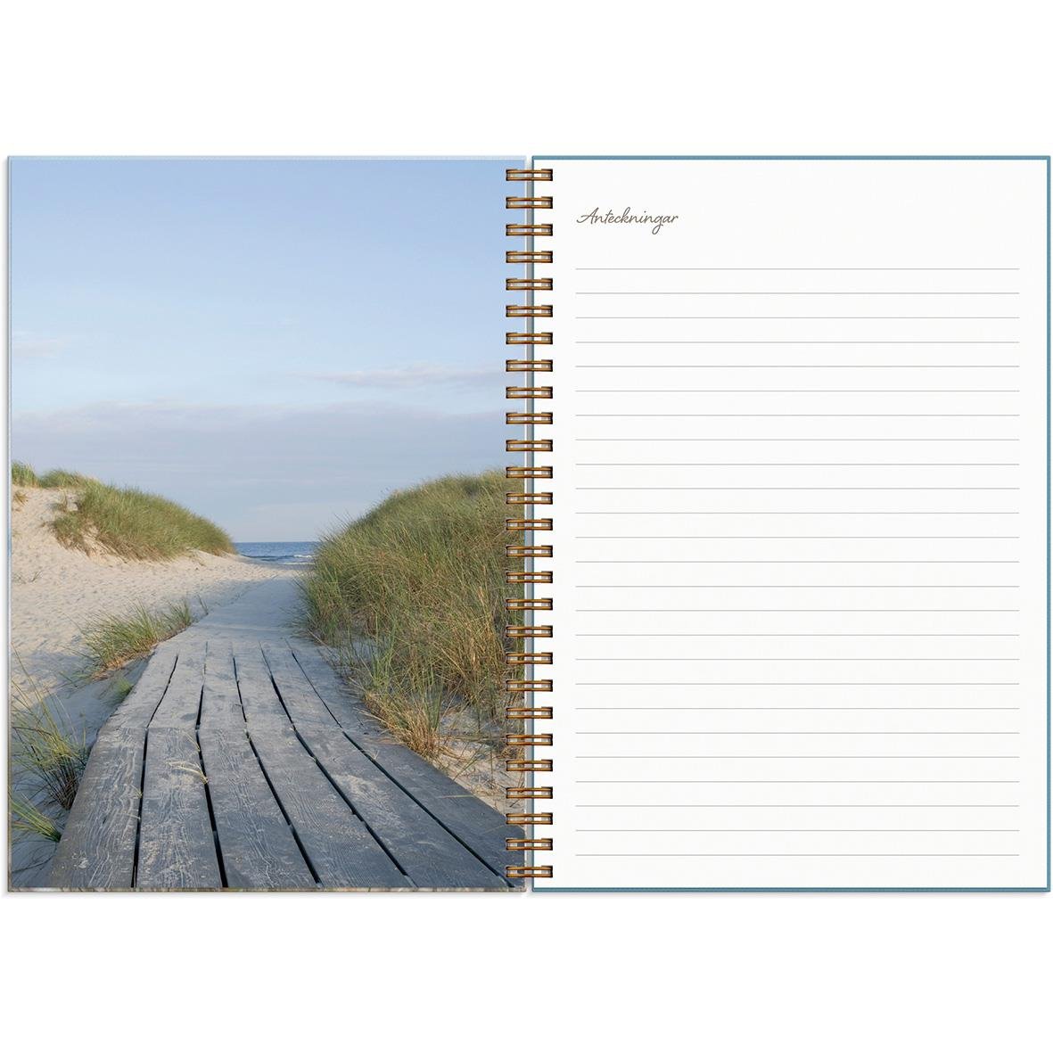 Öppnad almanacka med bild av en trästig på stranden och en sida för anteckningar