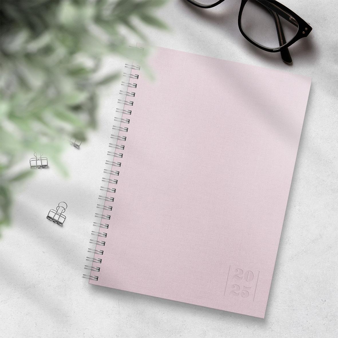 Rosa A5 almanacka med spiralbindning, glasögon och blommor på ett vitt bord