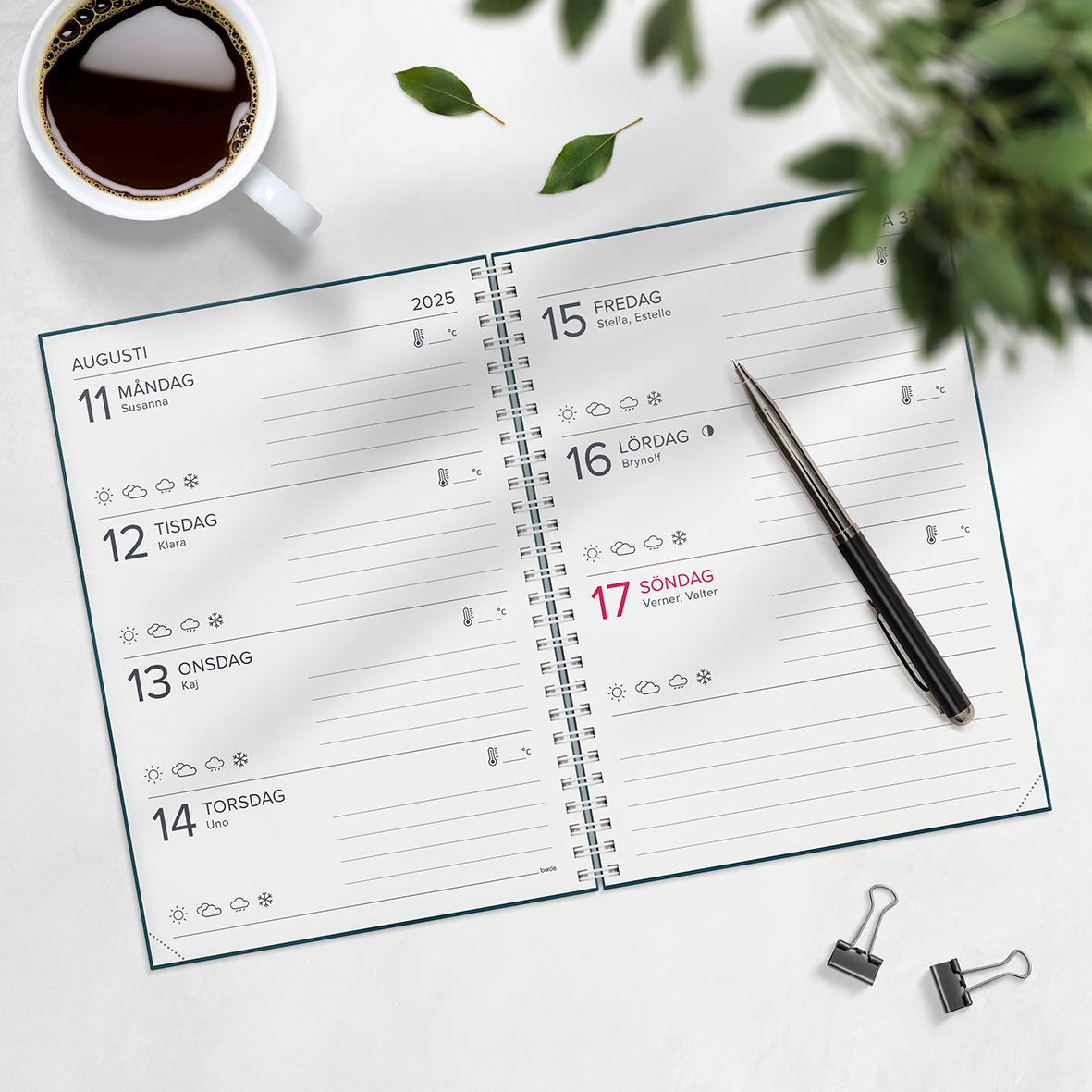 Öppen Almanacka Burde 1068 XL-Kalendern 2026 med penna, koppar och växtblad på bordet