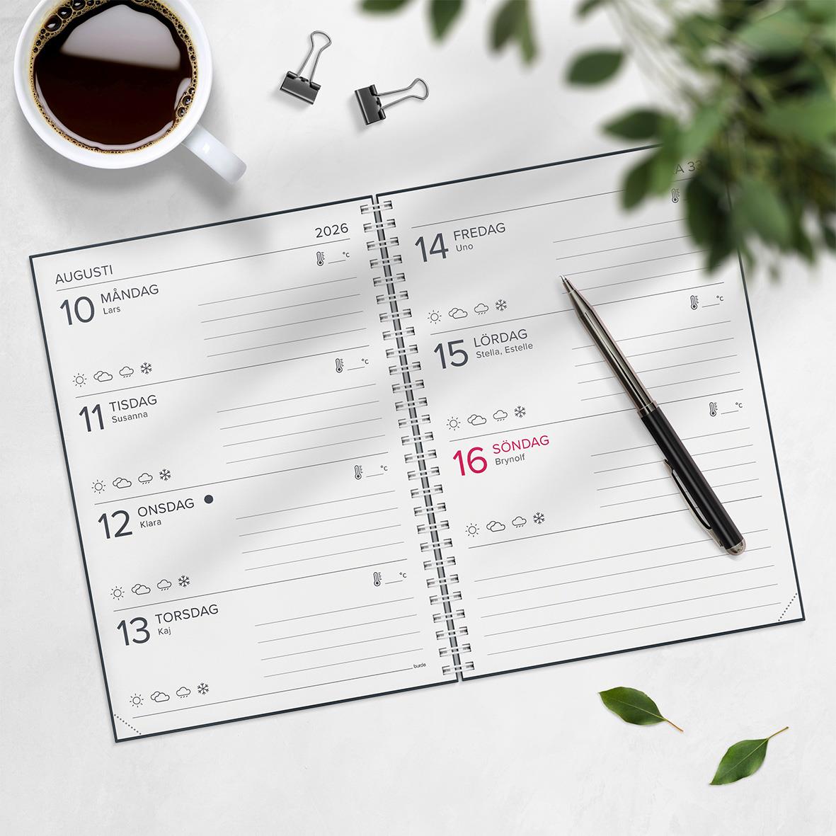 Öppen kalender för 2026 med datum och veckodagar, penna, kopp kaffe och gröna växter runt omkring