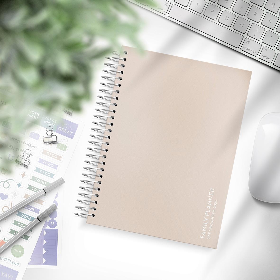 Familjeplanerare och kalender 2026 i A5-format med spiralbindning, omgiven av kontorsmaterial