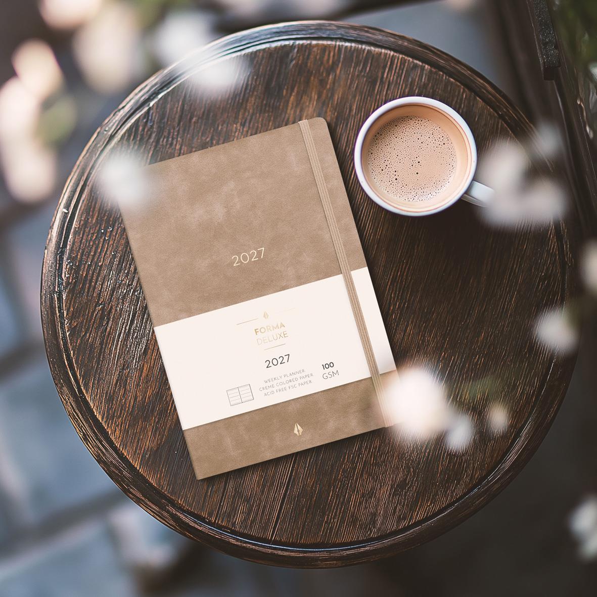 Brun Almanacka Burde 5967 Senator Forma Deluxe Mocka 2027 på rund träbord med kopp kaffe