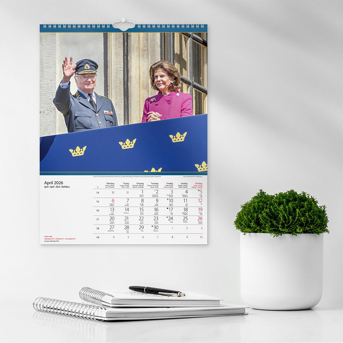 Väggkalender för 2026 med bild av kungafamiljen och en grön växt på en vit vägg