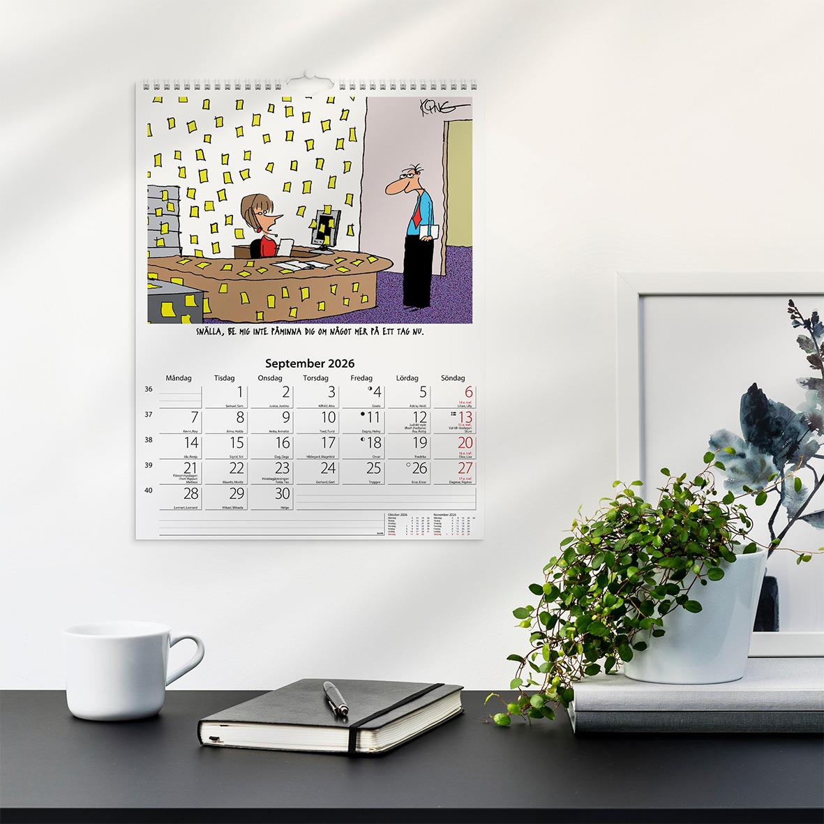 Väggkalender med kontorshumor för 2026, visar en tecknad scen med en person vid ett skrivbord och en annan som tittar in
