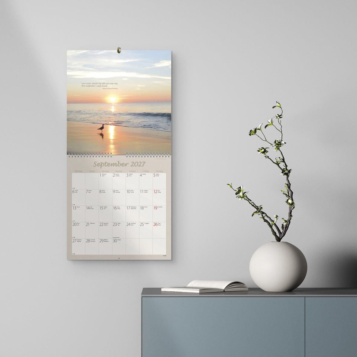 Väggkalender med motiv av en träbro och cyklister, för mars 2026, i beige och bruna toner