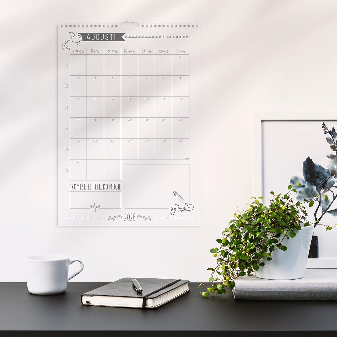 Väggkalender för augusti 2026 med doodle-design, placerad på vit vägg bredvid växt och skrivbord med kopp och anteckningsbok