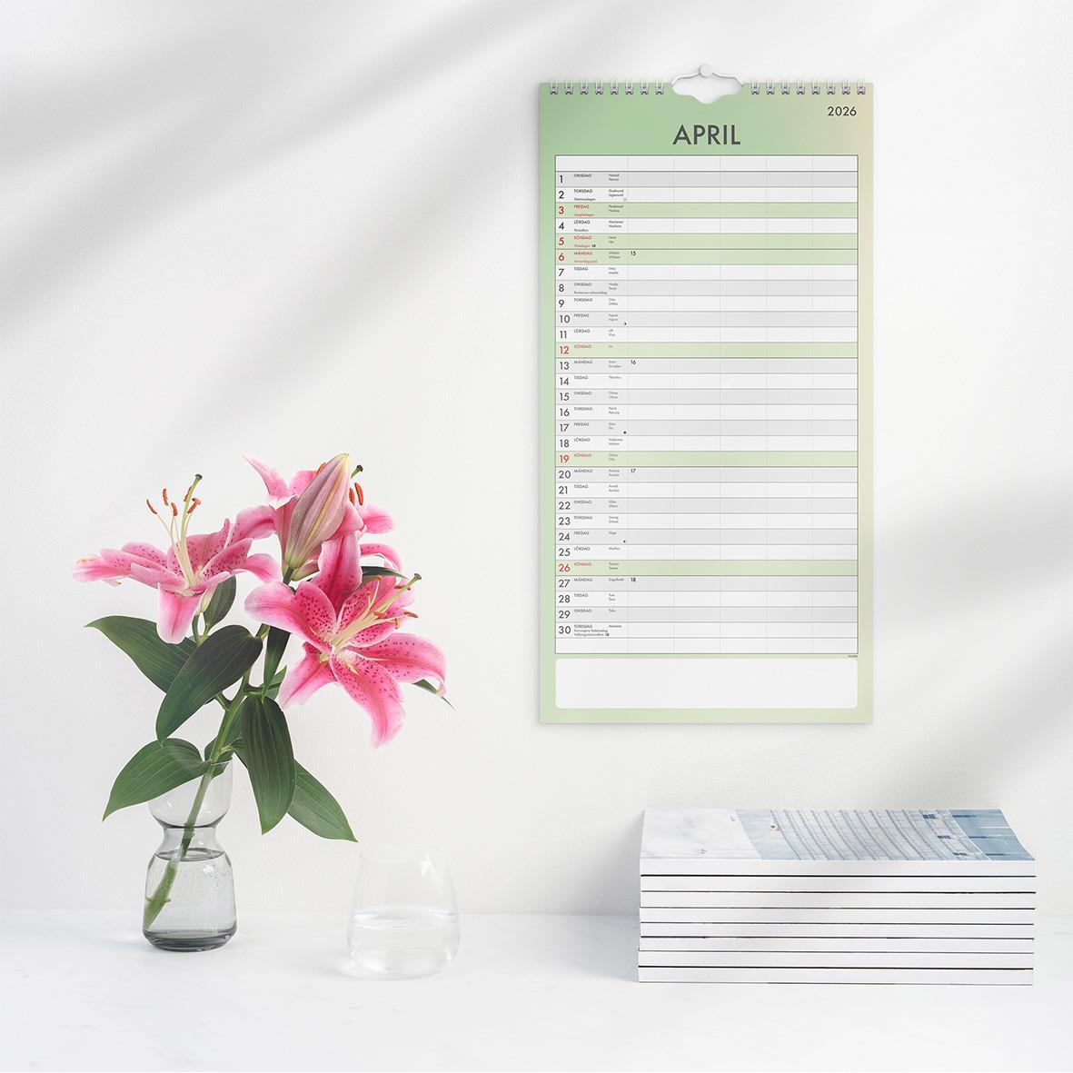 Väggkalender för april 2026 med tydlig layout, en blomsterbukett och en stapel med papper på en vit yta