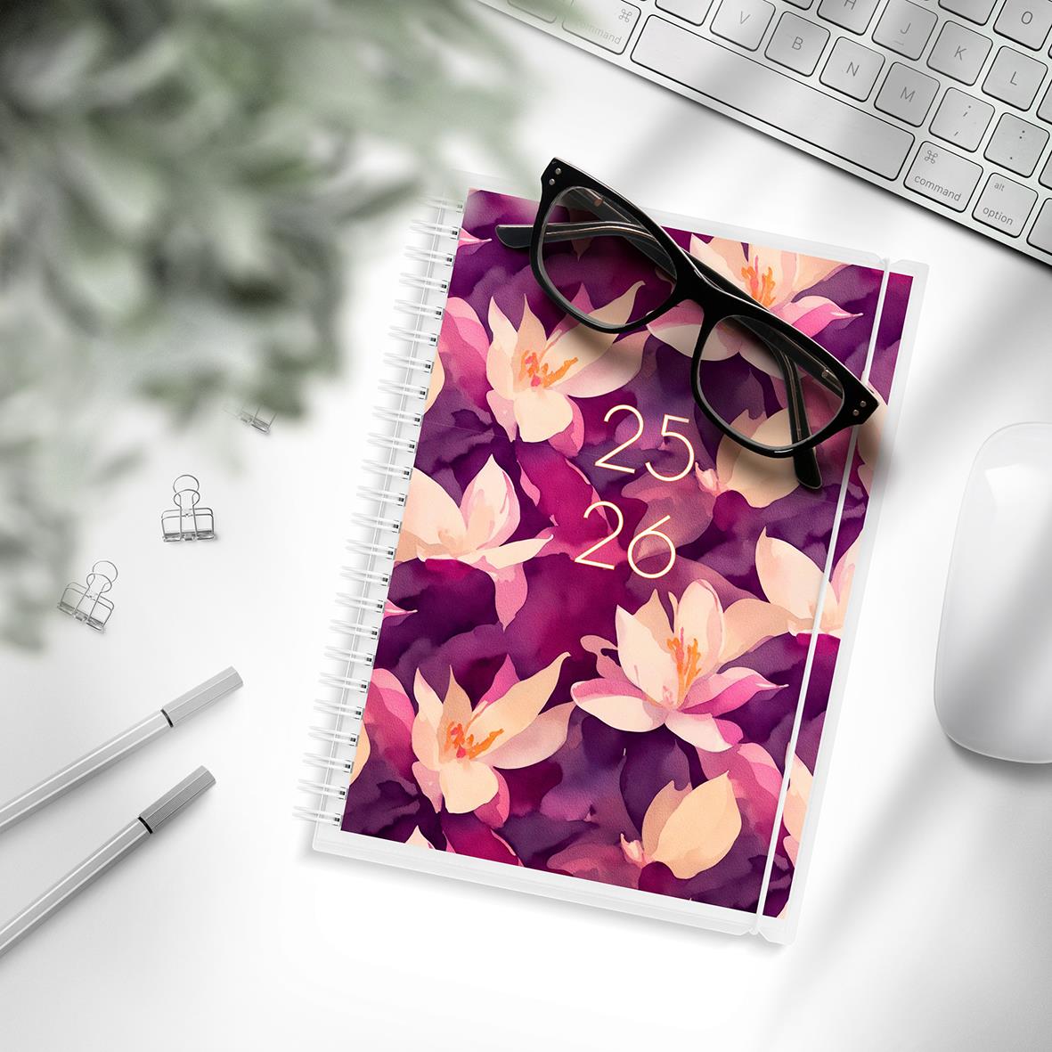 Studiealmanacka med blomsterdesign, glasögon, tangentbord, penn och mus på skrivbordet