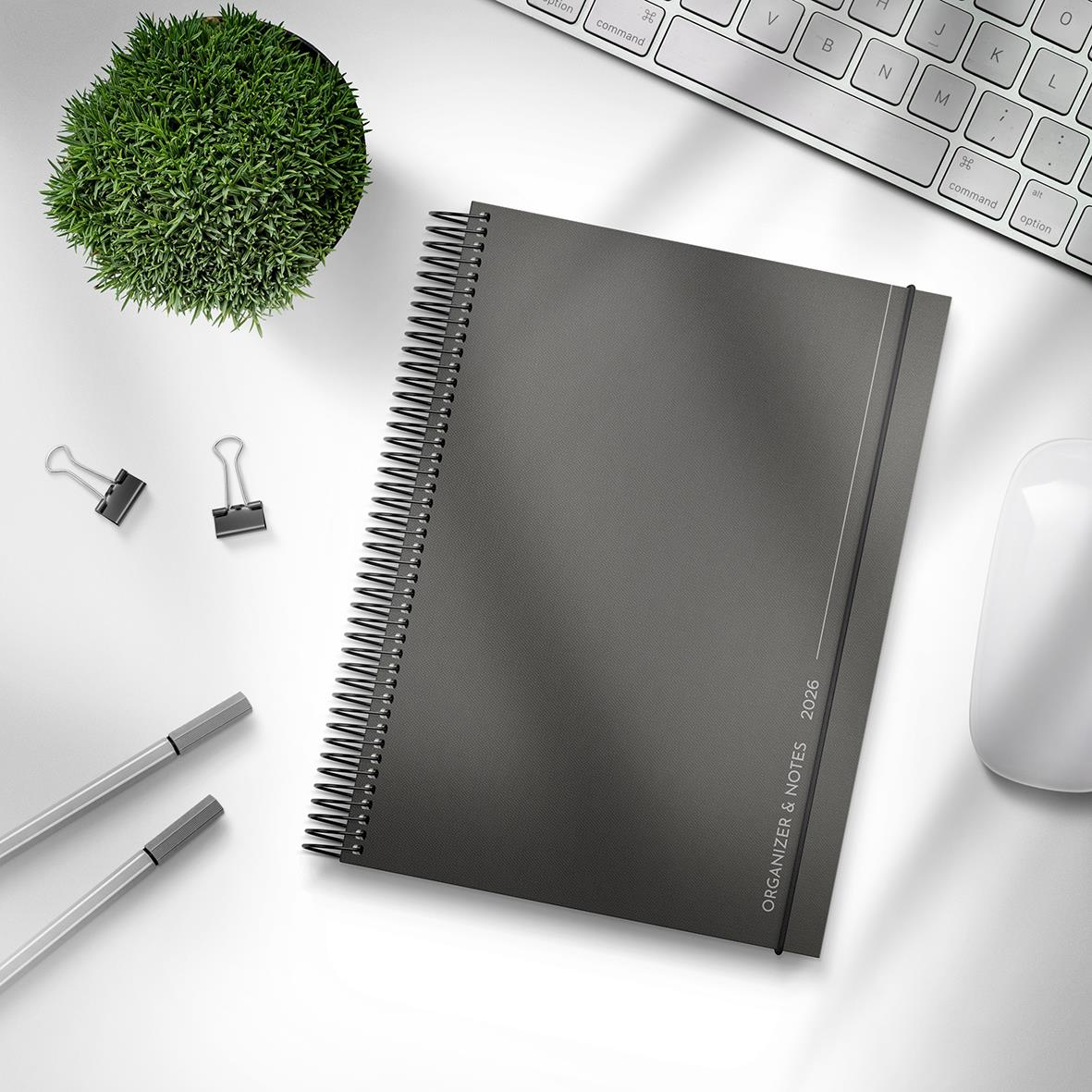 Svart almanacka Burde 1290 med spiralbindning, anteckningssidor 25-26, på skrivbord med tangentbord, mus, bläckpennor och växt