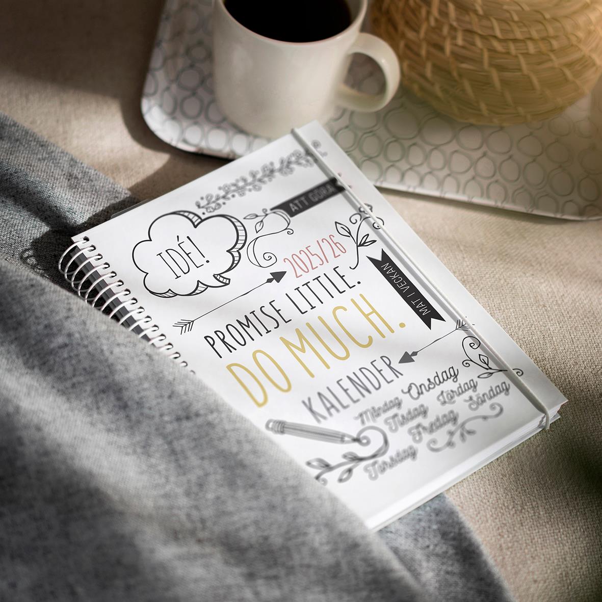 En kalender med doodle-illustration och text, en kopp kaffe och ett garnnystan på ett bord