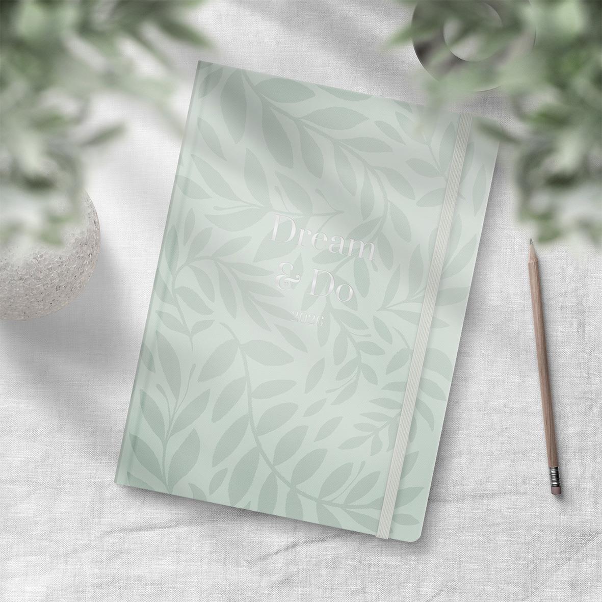 Ljusgrön planeringsbok med bladmönster och texten Dream & Do 2026 på omslaget, placerad på vit yta med penna bredvid