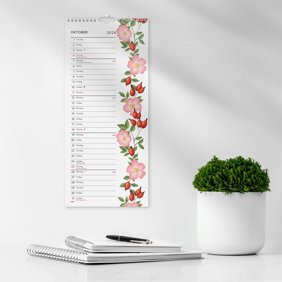 Väggkalender för oktober 2026 med blomsterdesign och plats för anteckningar, på skrivbord framför en växt