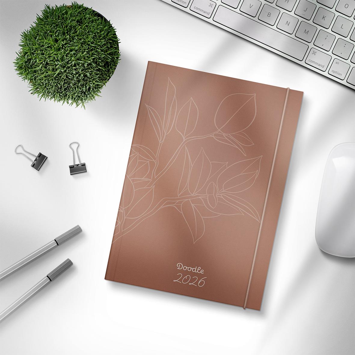 Årsalmanacka Burde 1219 Doodle 2026 med rosa omslag och bladmotiv, omgiven av kontorsmaterial