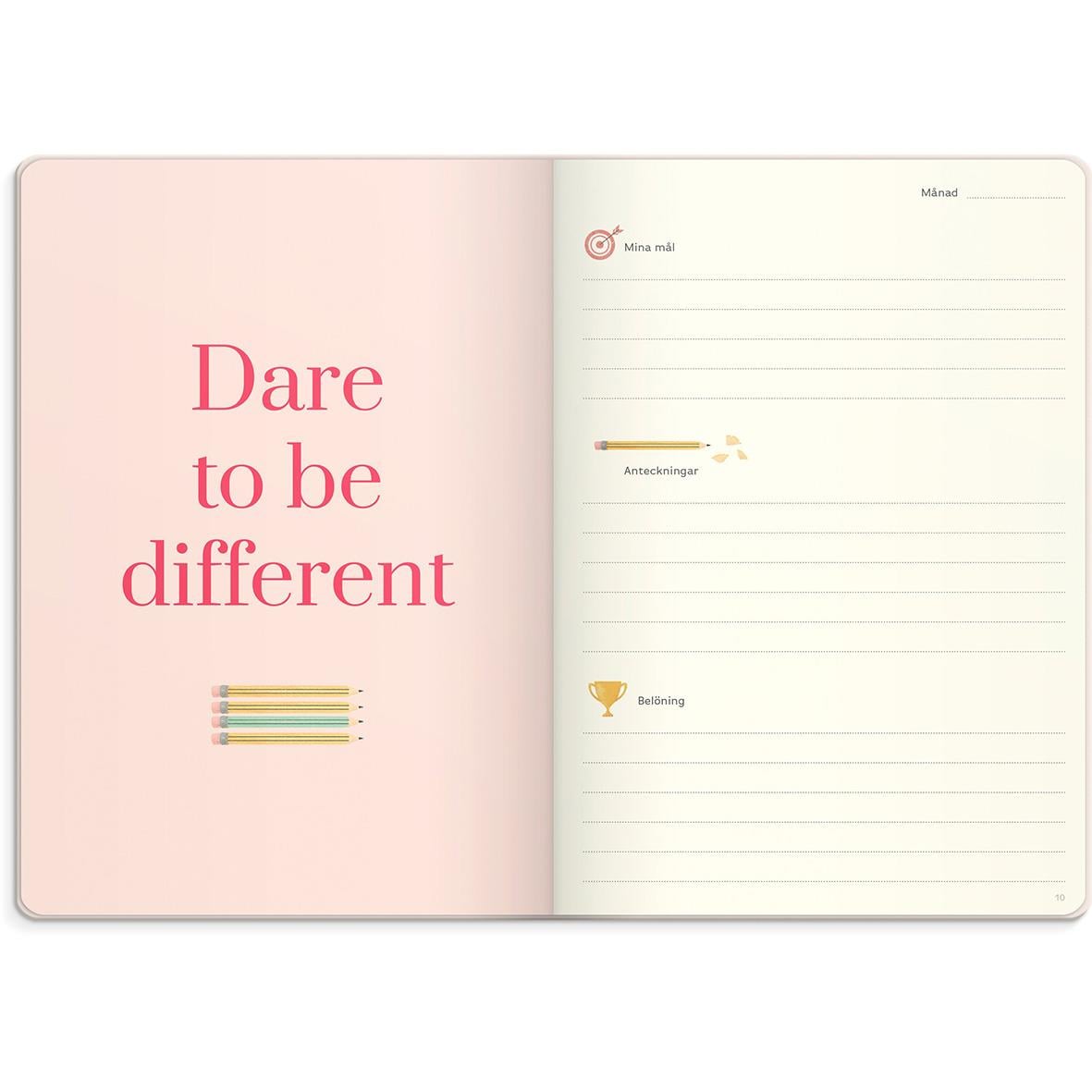 Öppnad almanacka med rosa och beige sidor, text Dare to be different och linjer för anteckningar