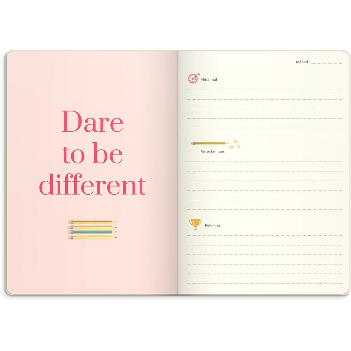 Öppnad almanacka med rosa och beige sidor, text Dare to be different och linjer för anteckningar
