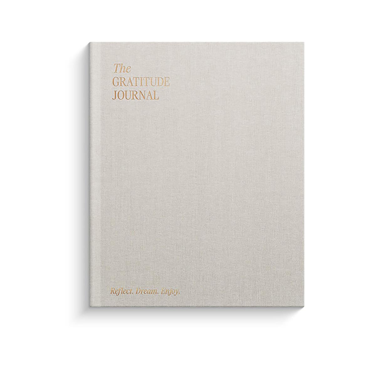 En ljusgrå anteckningsbok med titeln The Gratitude Journal i guldtext
