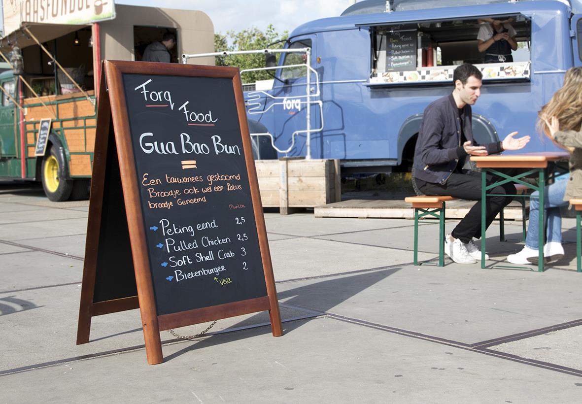 " med svart griffeltavla för matmeny utomhus, med människor och food trucks i bakgrunden"