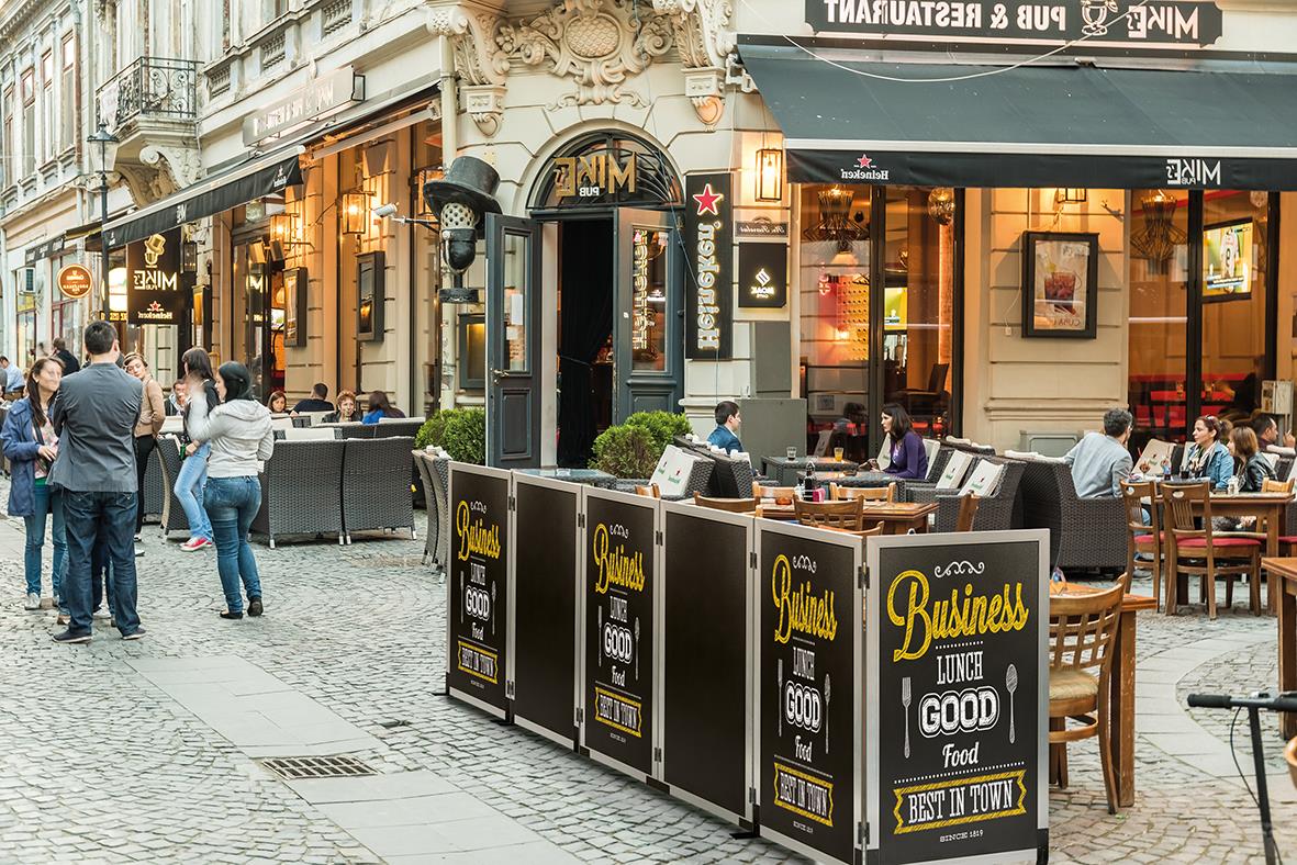 Uteservering med multiboard i rostfritt stål på en stadsgata med människor och butiker i bakgrunden