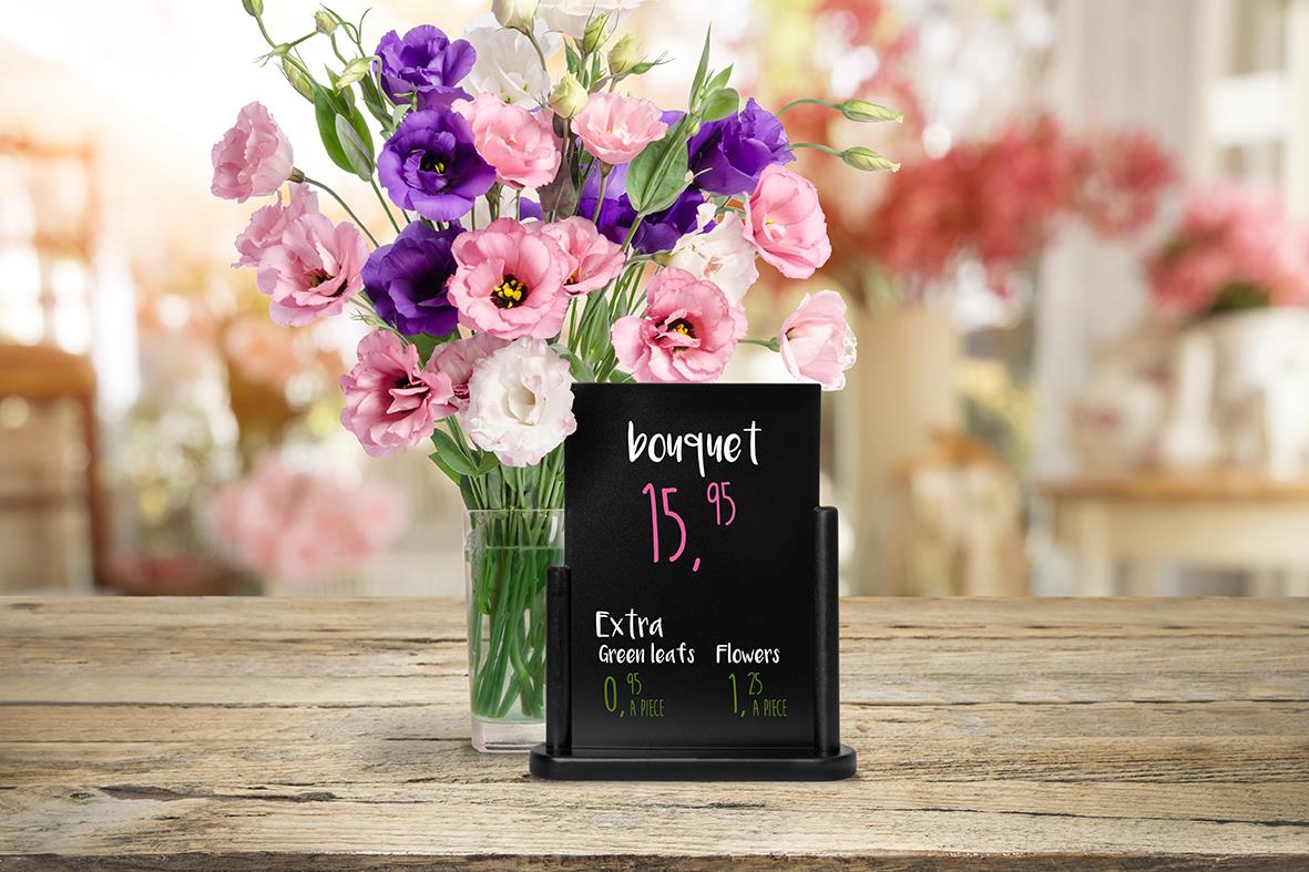 Svart griffeltavla med blomsterarrangemang och prisetikett på bordet