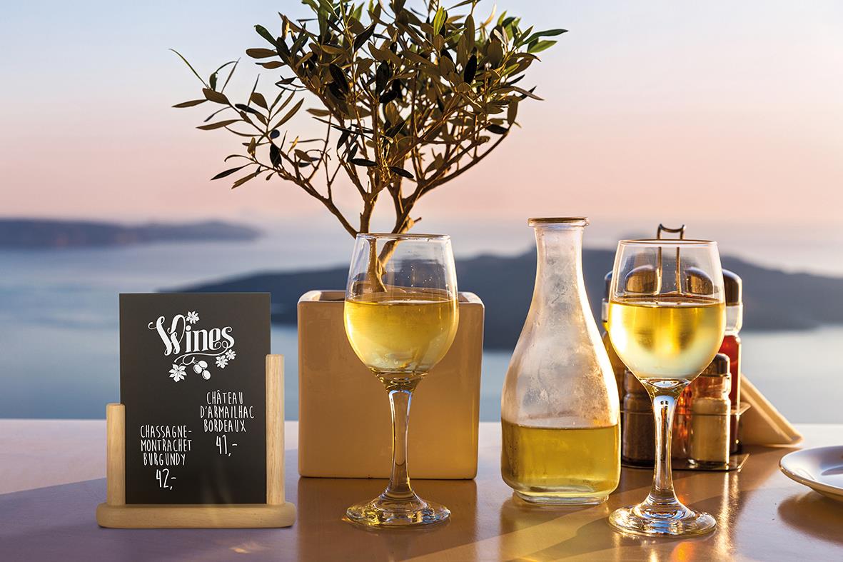 Vinglas, vattenkanna och bordsskylt på uteplats med hav i bakgrunden