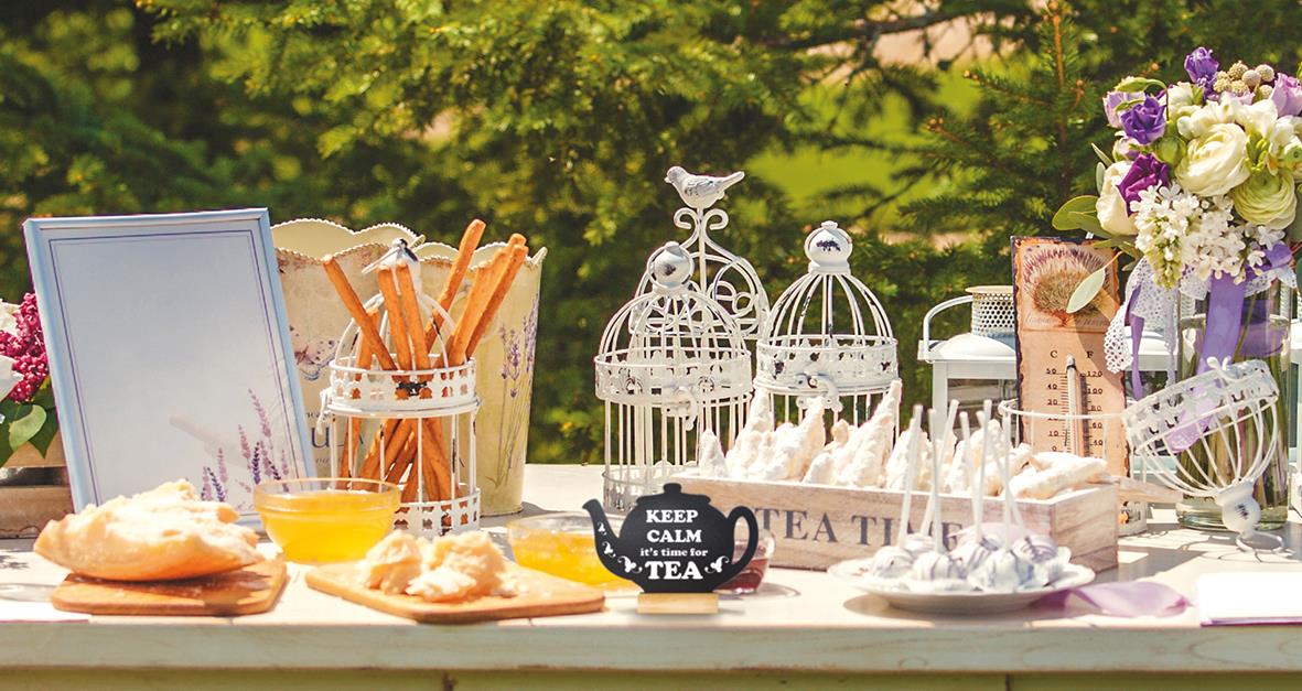 Utomhusbord med griffeltavla, tekanna, fågelbur, blommor och frukost i solsken