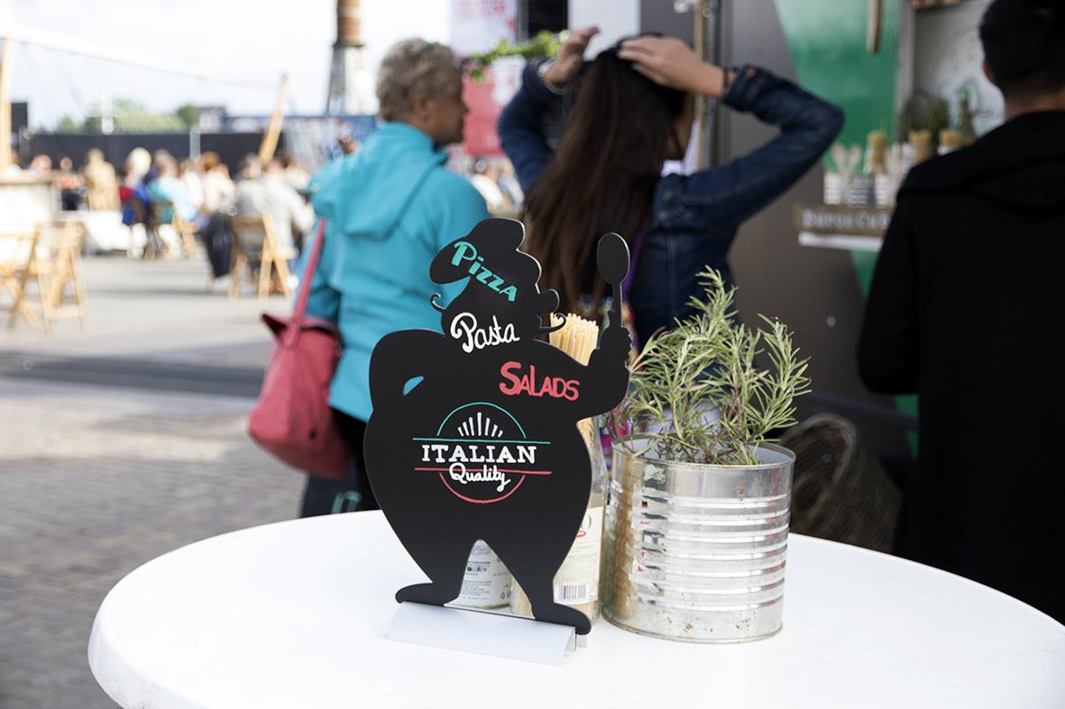 Griffeltavla i form av en hund med meny för pizza, pasta, sallad och italiensk mat, placerad på ett bord utomhus