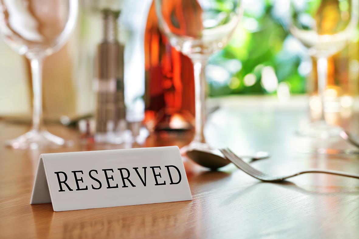 Bordsskylt Reserved i akryl på ett bord med glas och bestick i bakgrunden