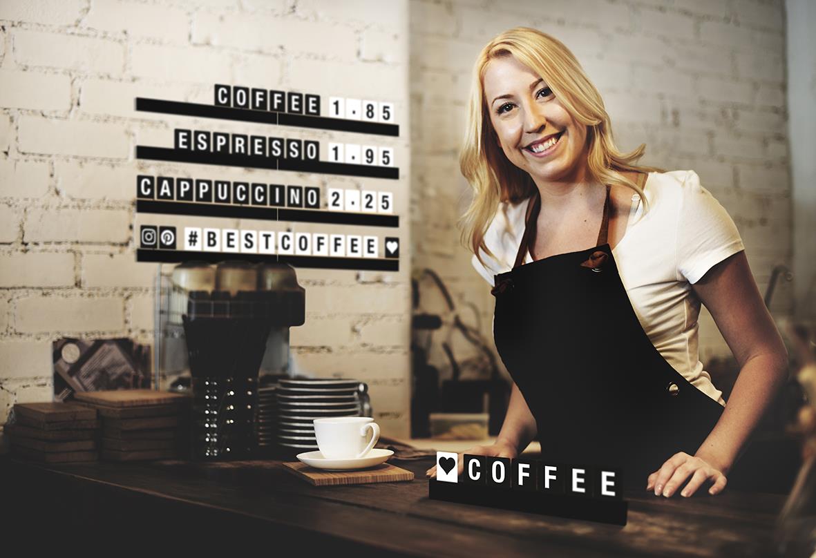 Kvinna bakom kaffebar med svart bokstavshylla och skyltar med kaffepriser