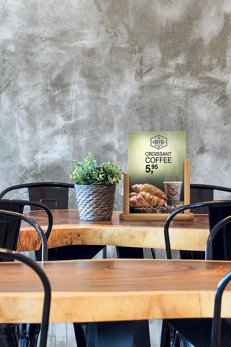 " med grå betongstruktur, bord med växt i kruka och reklamskylt för croissant och kaffe i ett café."