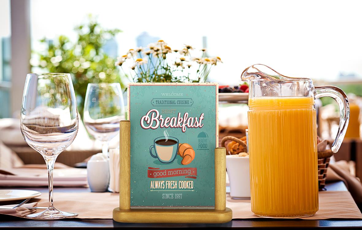 " med glas, juice och ett bordskort med texten Breakfast på ett soligt bord"