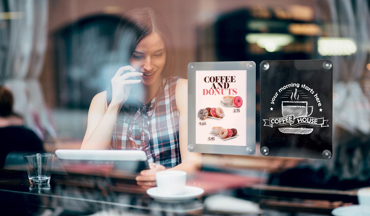 Kvinna tittar på en digital meny i ett café, syns genom ett fönster med skyltar om kaffe och bakverk