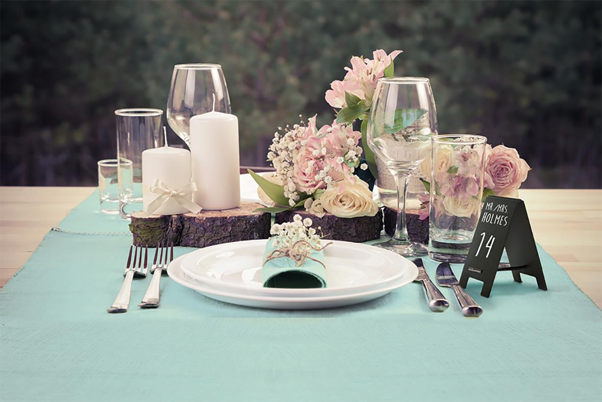 Borddukning med glas, ljus, blommor och tallrik på bord med blå duk