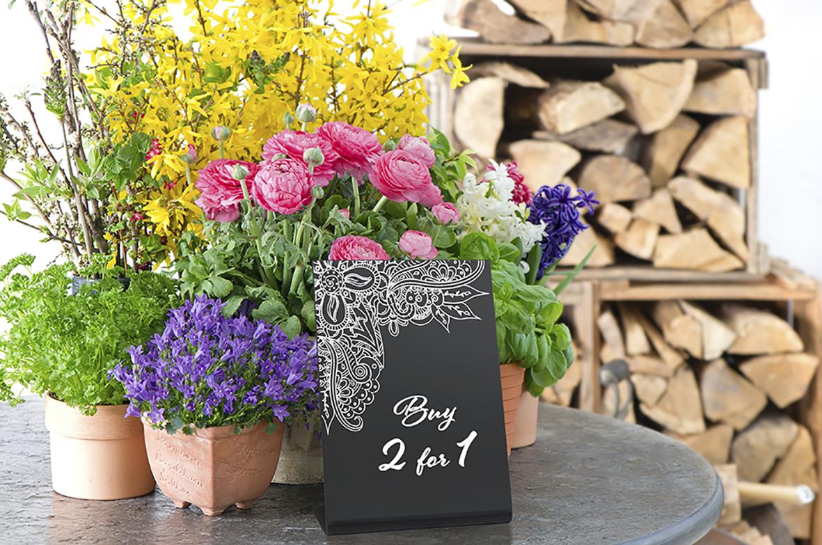 Svart griffeltavla med vitt textbudskap och blomsterarrangemang på bord