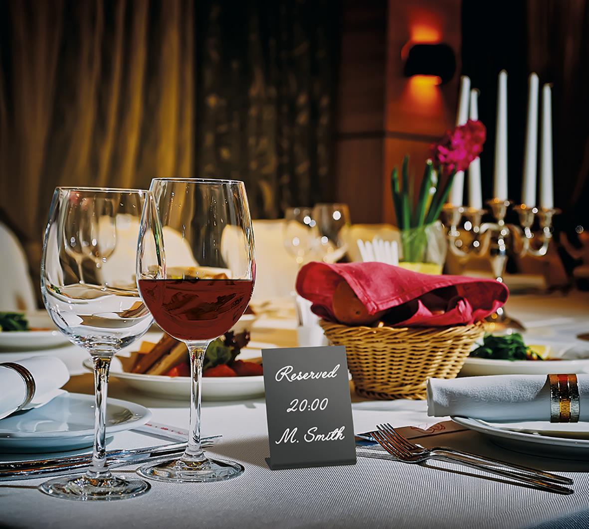 Elegant middagsbord med glas, vin, blomster och reserverad skylt för middag