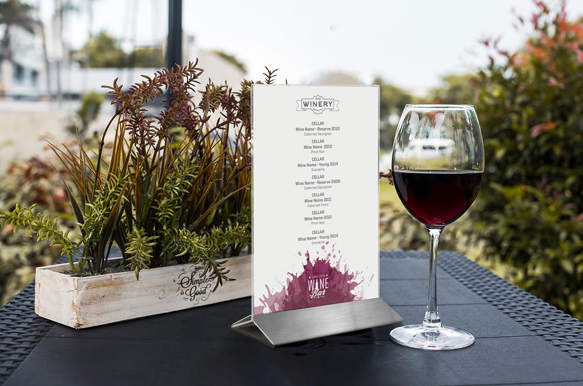 Vitt blomsterarrangemang, vinlista och ett glas rödvin på bord utomhus