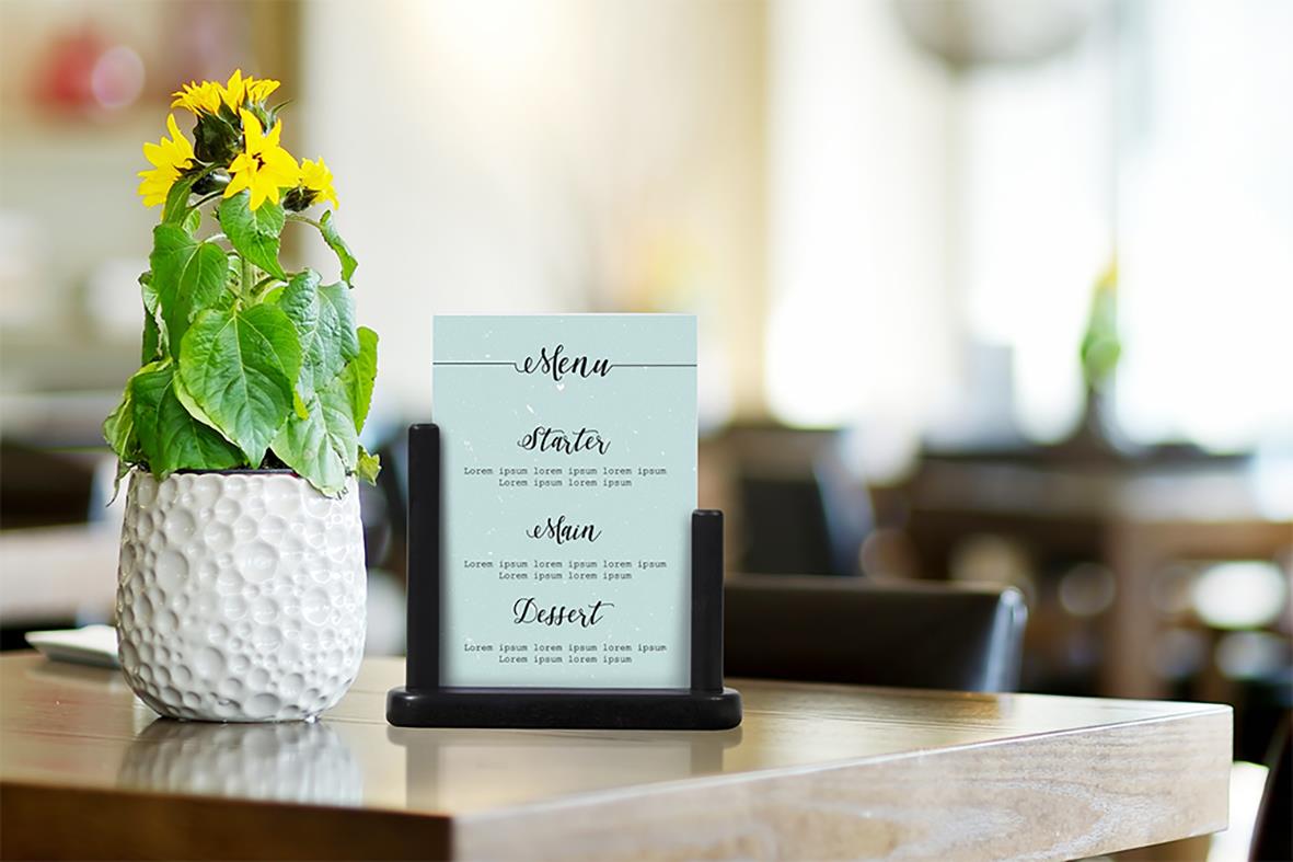 Menykort på bordet med blomkruka och restaurangnamn i bakgrunden