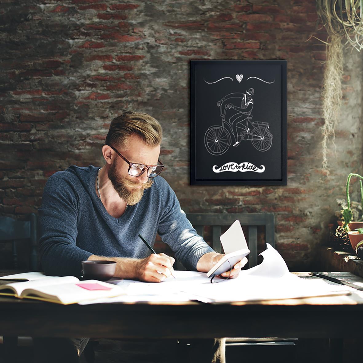 Man skriver på en svart griffeltavla med cykelmotiv och text Love & Ride, i ett rum med tegelvägg och växter
