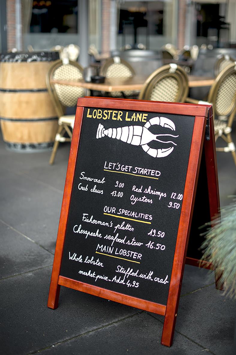 Lobster Lane meny skylt utomhus med rätter som hummer, räkor och ostron, samt specialiteter som hummerfiskarens tallrik och hel hummer.
