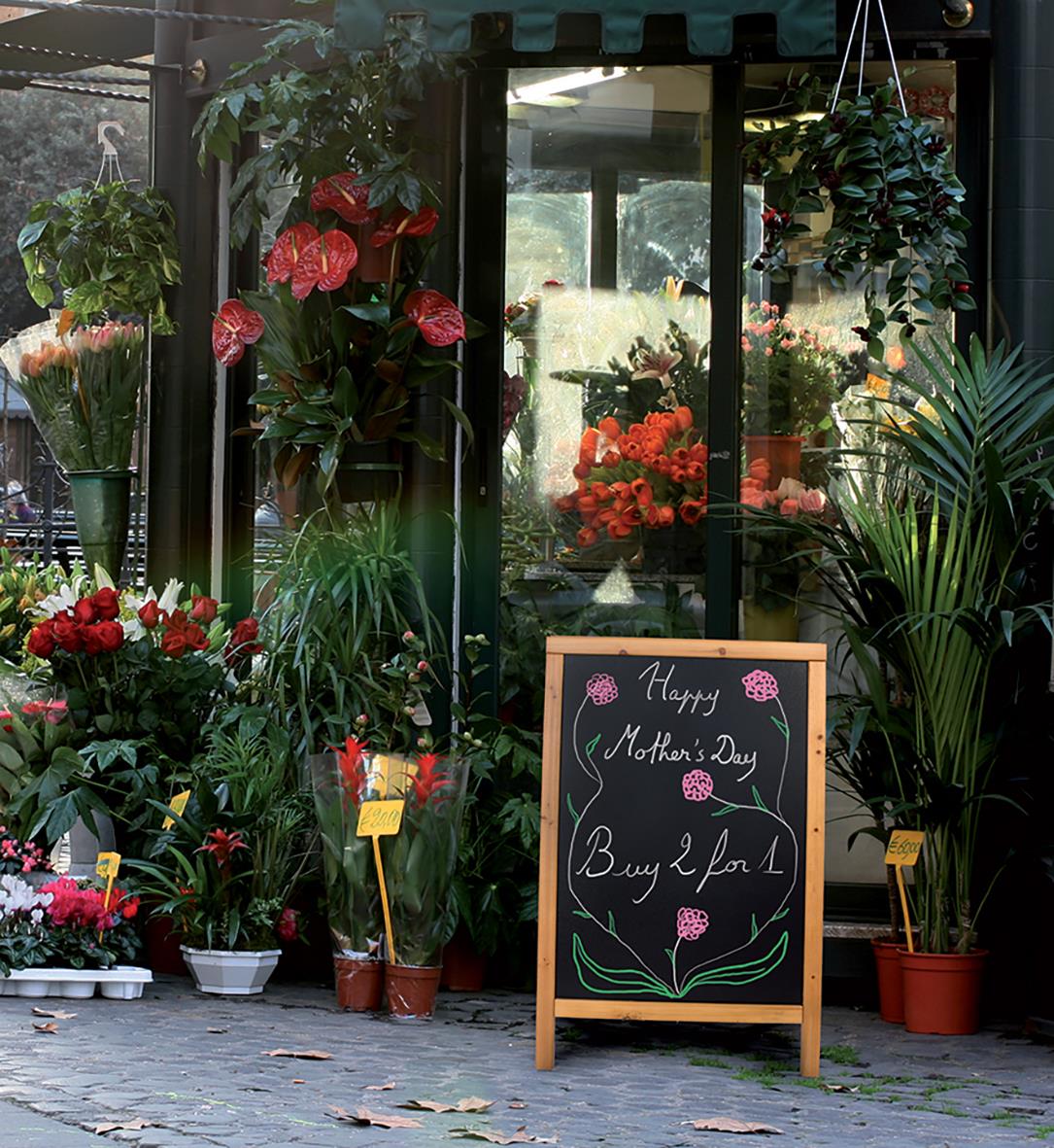 Blomsterbutik med blomster och en svart anslagstavla med texten Happy Mothers Day Buy 2 for 1