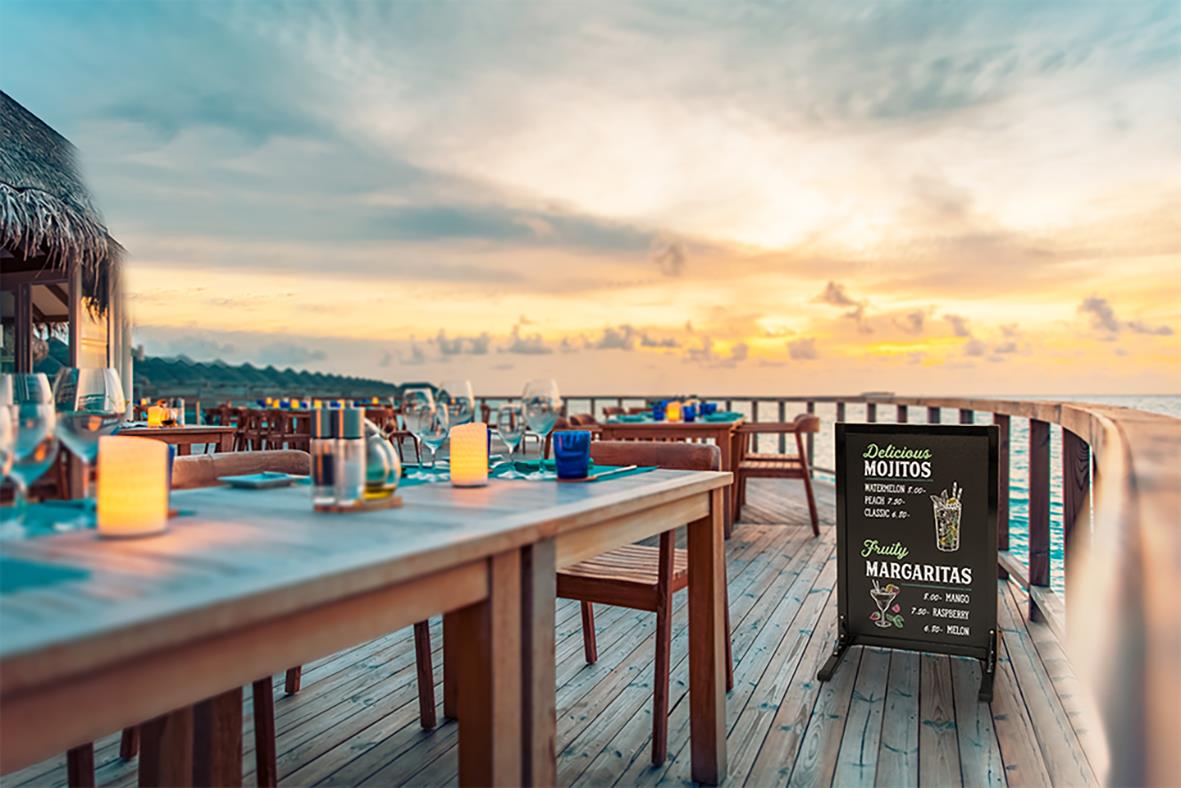 Uteservering med bord, stolar och skylt med meny vid solnedgång