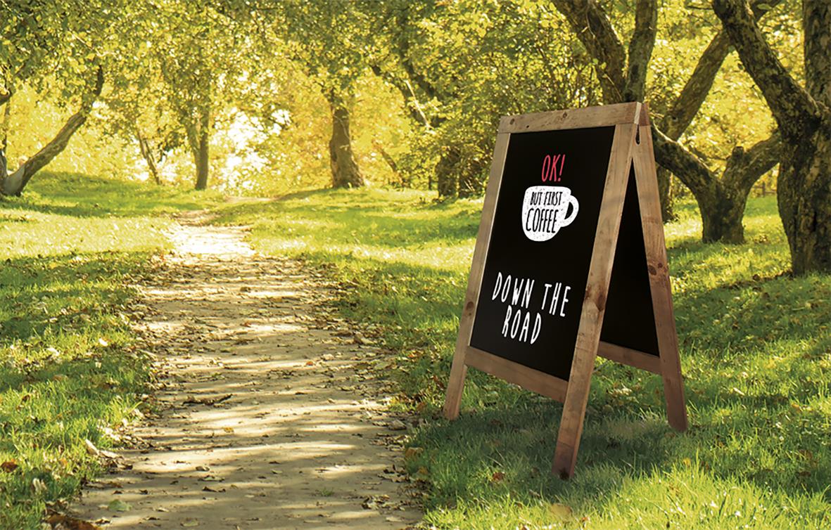 Väg i naturmiljö med träd och en svart anslagstavla med text