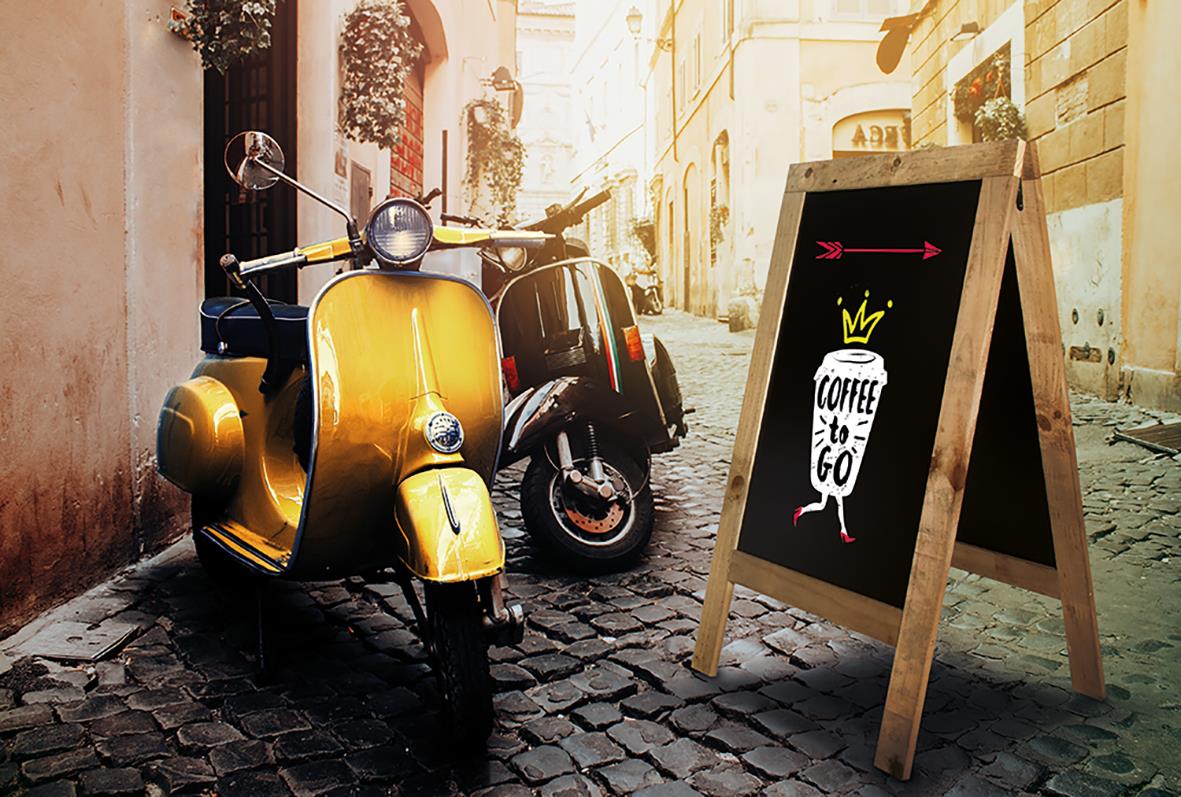 Gatuställ med svart anslagstavla och två vintage mopeder på en kullerstensgata