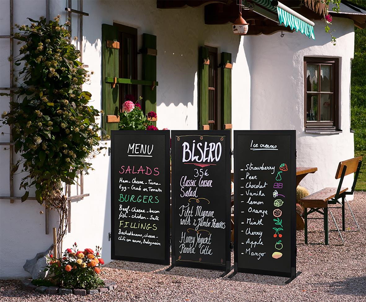 Utomhusmenystavlor för restaurang med meny och drinkar, omgiven av blommor och en vit byggnad