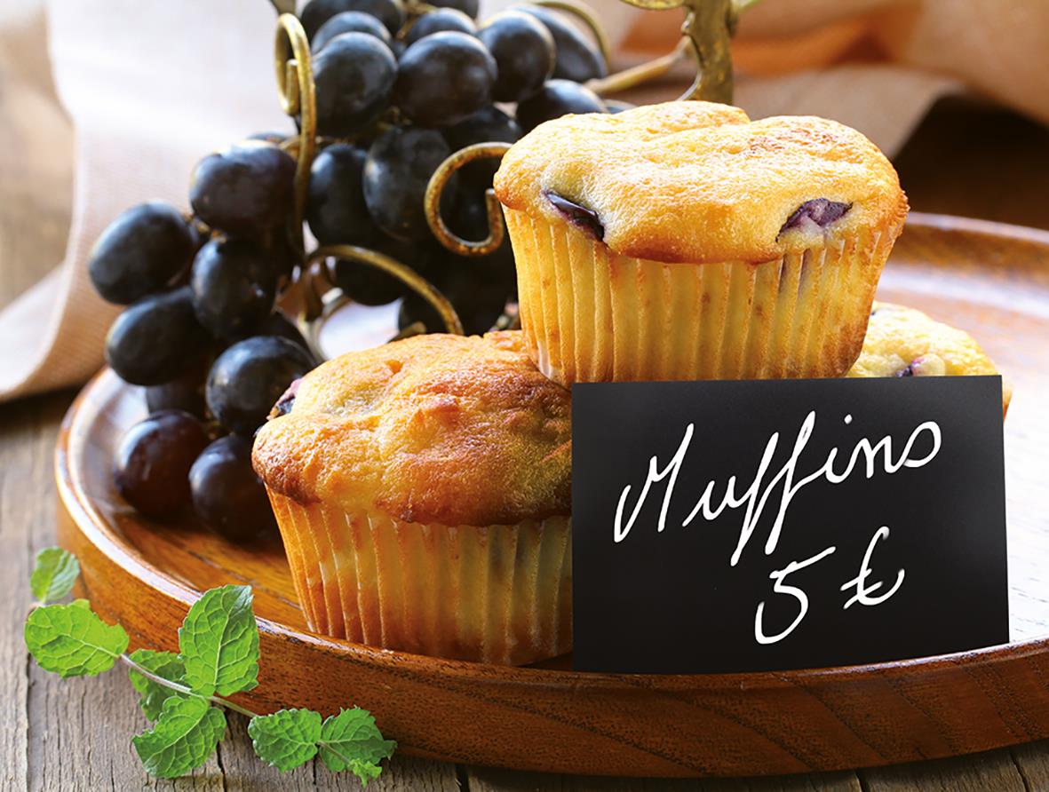 Två muffins på en träbricka med ett svart skylt som säger Muffino 5 € och druvor i bakgrunden