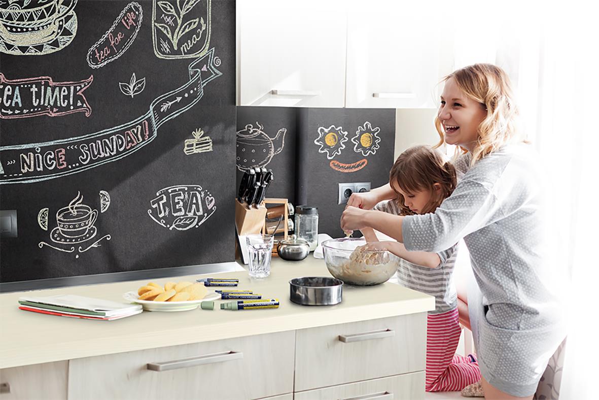 " och vuxen målar på köksvägg med svart griffeltavelfärg, använder kritor och penslar"